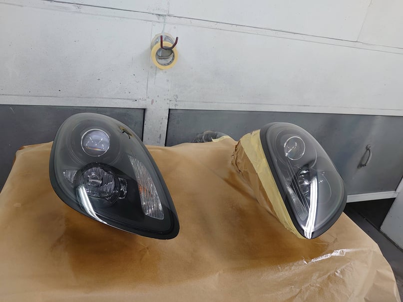 a pair of porsche headlights sitting on top of a piece of paper being customized with black tint, in cardiff bodyshop doing car body repairs